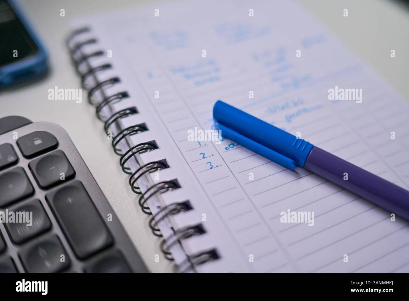 Un stylo à couvercle bleu sur un cahier blanc à côté d'un ordinateur sur un bureau, avec 1 2 3 écrit sur le livre. Banque D'Images