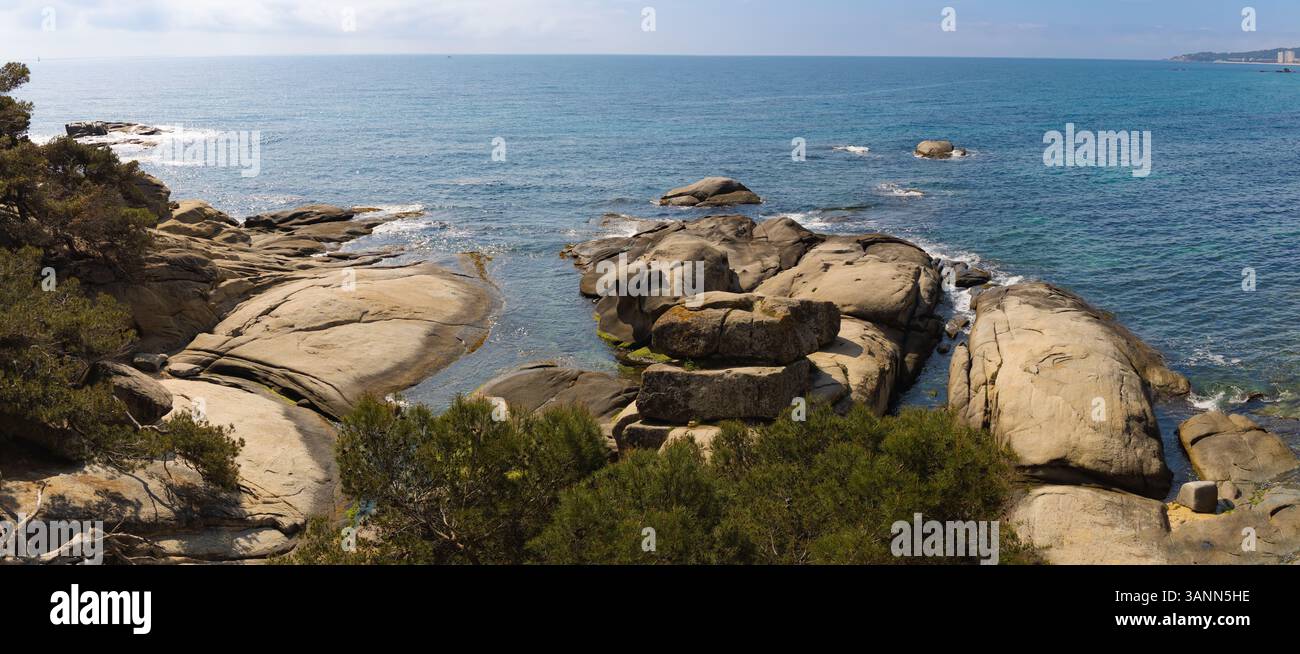 Vue panoramique à grand angle de Punta Rocas planes, Costa Brava, mettant en valeur les roches lisses uniques, la mer bleue et les pins au premier plan. Banque D'Images