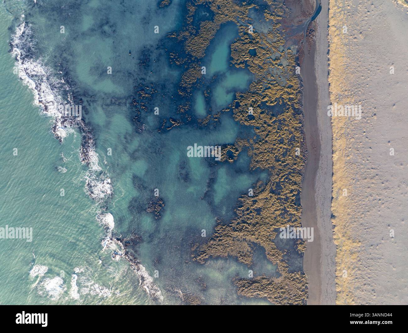 Vue aérienne de belles vagues turquoises de l'océan s'écrasant sur une plage de sable immaculée avec un littoral accidenté, Selfoss, Islande. Banque D'Images