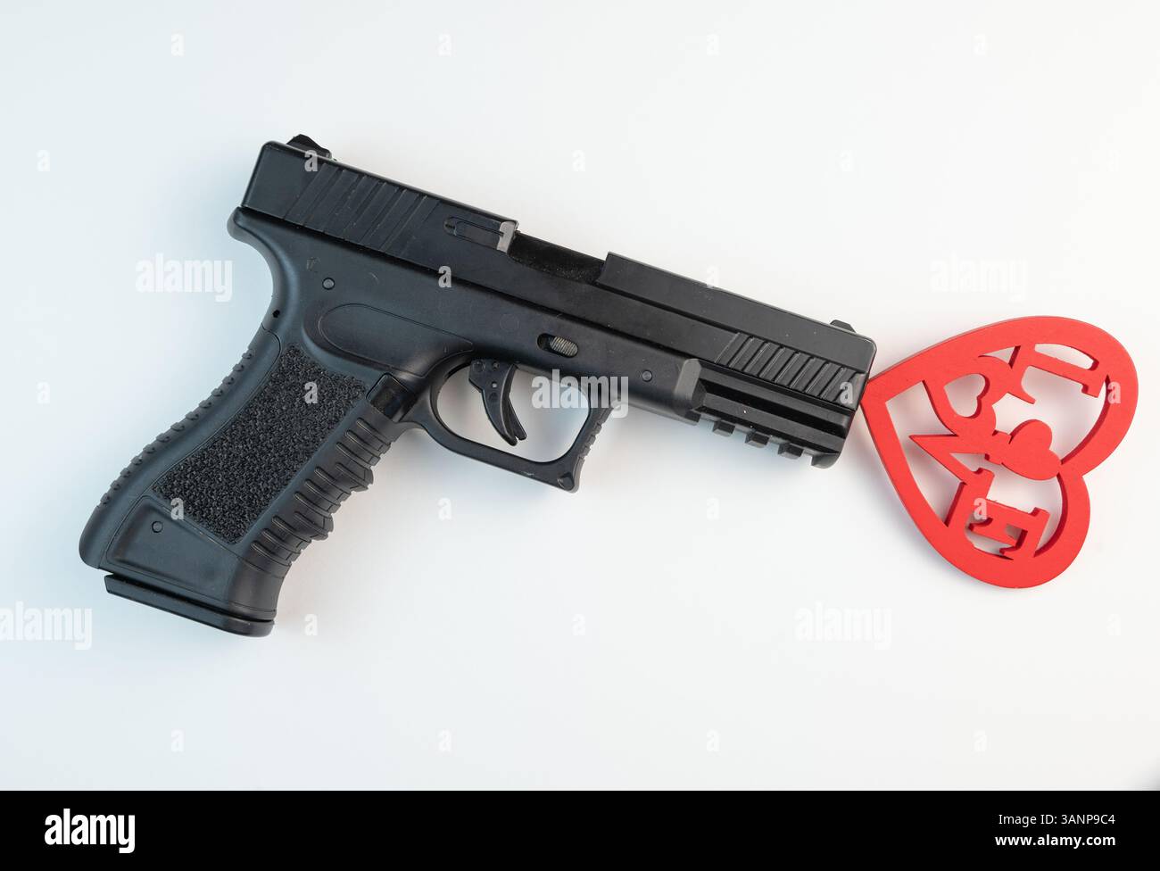 Une juxtaposition saisissante d’une arme de poing et d’un symbole de cœur rouge, mettant en lumière les thèmes de l’amour et de la violence. Banque D'Images