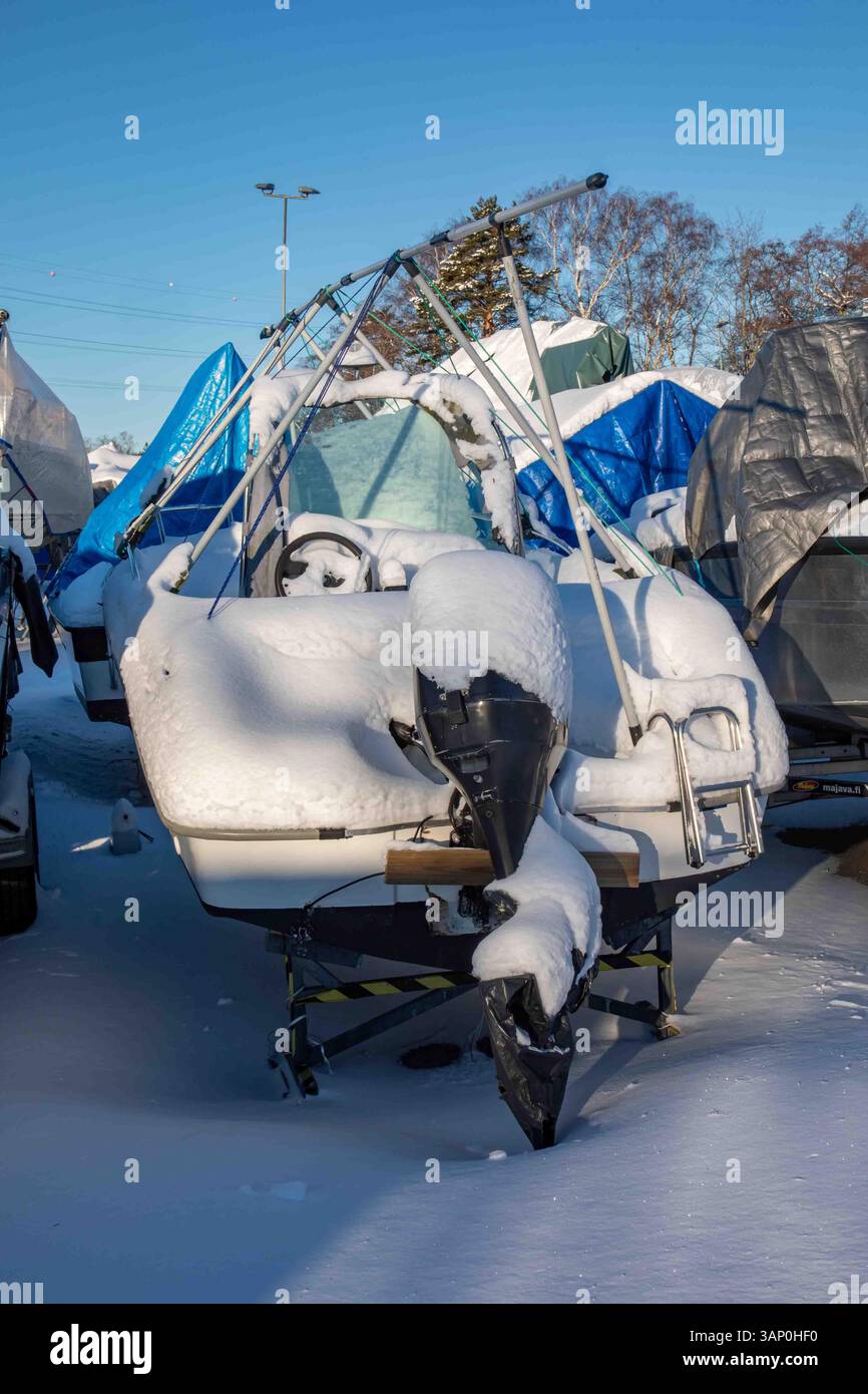 Bateau recouvert de neige avec moteur hors-bord au quai de stockage hivernal Rajasaari dans le district de Taka-Töölö à Helsinki, Finlande Banque D'Images