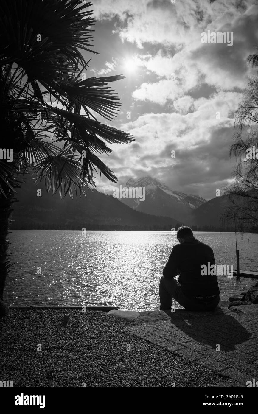 Un homme est assis à l'arrière-plan du soleil sur la rive du lac Walen devant les montagnes enneigées des Alpes de Glaris, en Suisse Banque D'Images