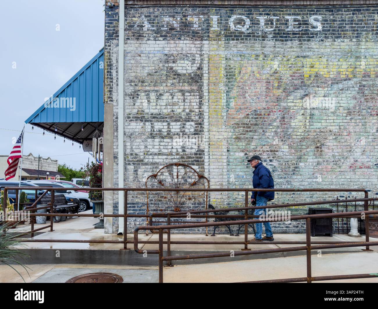Homme dans ses années 80 promenades se sont escamotées sur le trottoir devant le vieux mur peint en briques du magasin d'antiquités dans le quartier historique du centre-ville de Smithville, Texas, États-Unis. Banque D'Images