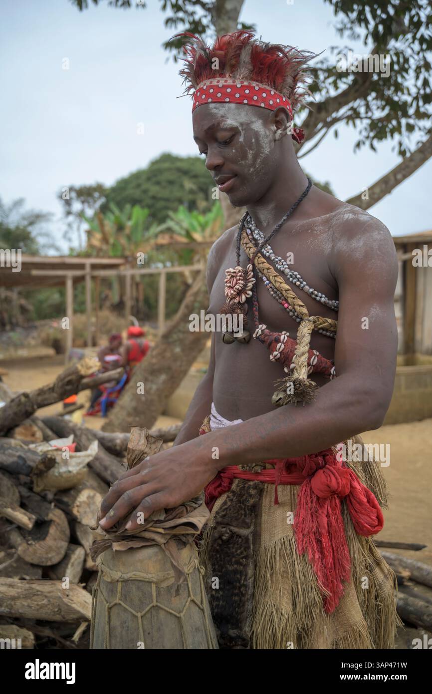 Portrait d'un batteur fixant son tom-tom , vêtu d'un costume rituel fait de peaux d'animaux et de plumes, un matin après une cérémonie toute la nuit. Banque D'Images