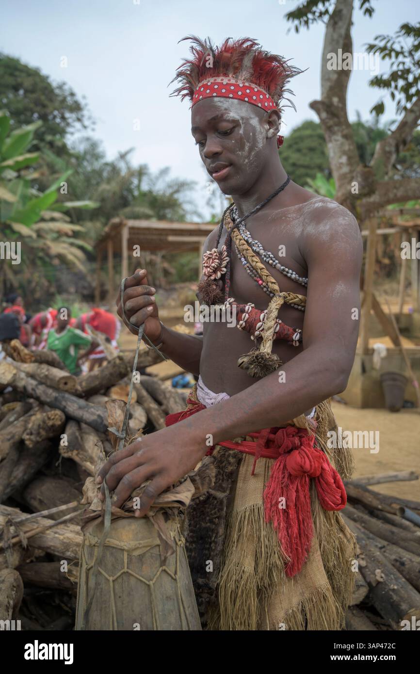 Portrait d'un batteur fixant son tom-tom , vêtu d'un costume rituel fait de peaux d'animaux et de plumes, un matin après une cérémonie toute la nuit. Banque D'Images
