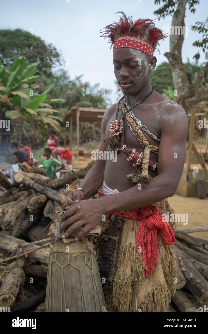 Portrait d'un batteur fixant son tom-tom , vêtu d'un costume rituel fait de peaux d'animaux et de plumes, un matin après une cérémonie toute la nuit. Banque D'Images