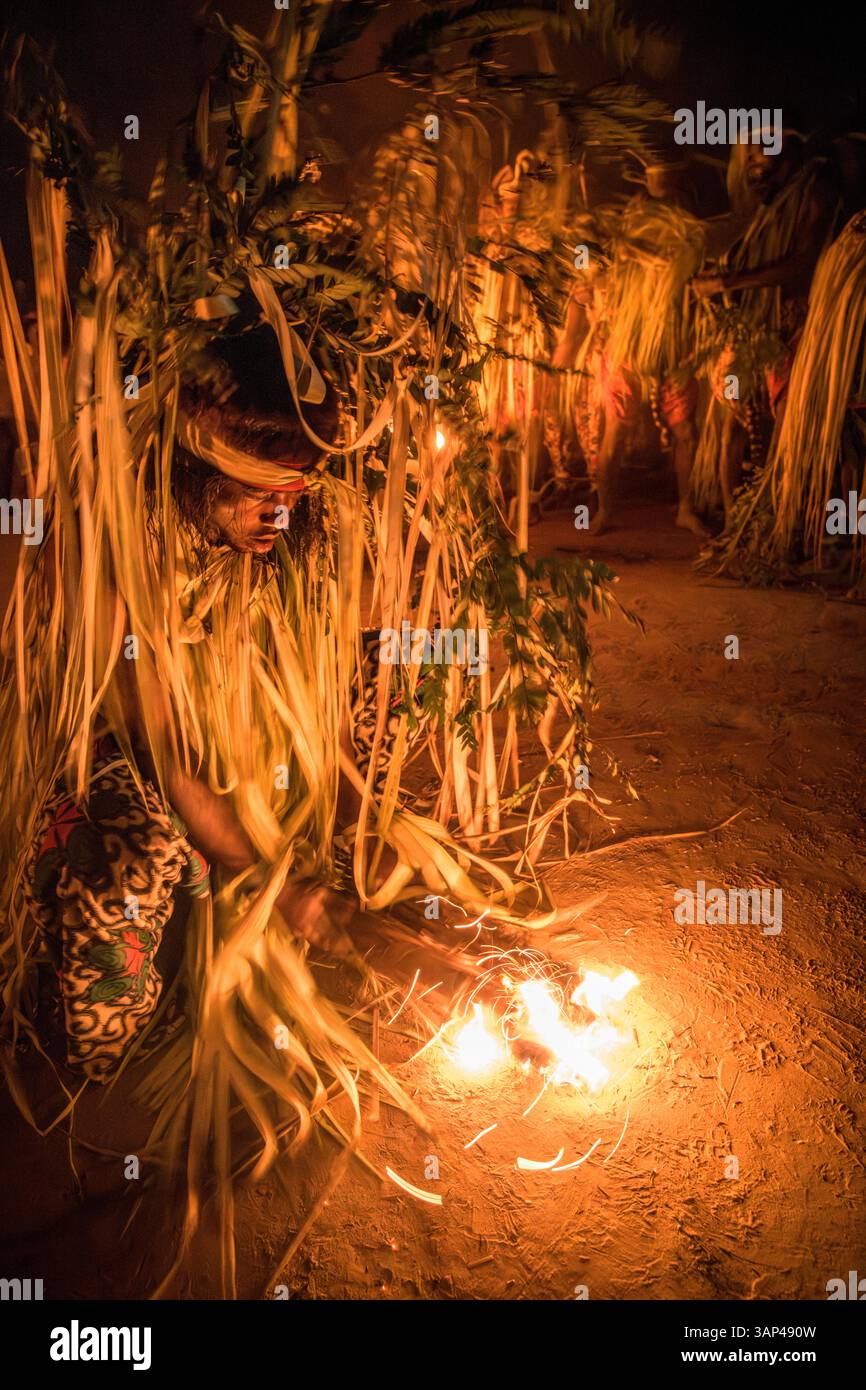 Participant à une cérémonie Bwiti, vêtu d'un costume rituel fait de feuilles de palmier séchées, préparant le feu pour commencer sa danse. Banque D'Images