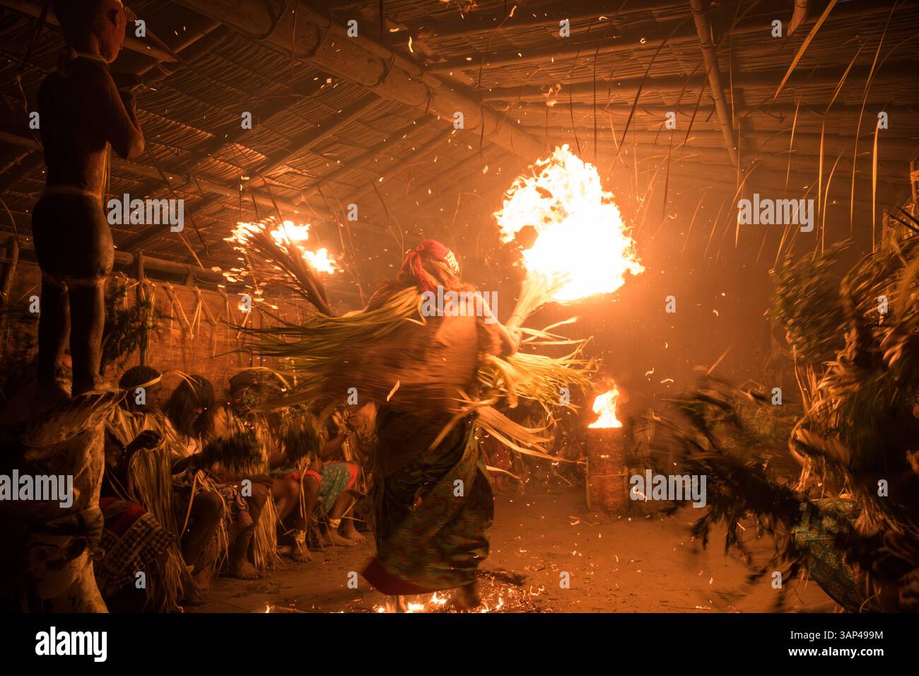 Les participants à une cérémonie des Bwiti, vêtus d'une tenue rituelle faite de feuilles de palmier séchées, dansent avec des torches allumées à l'intérieur d'un petit temple. Banque D'Images