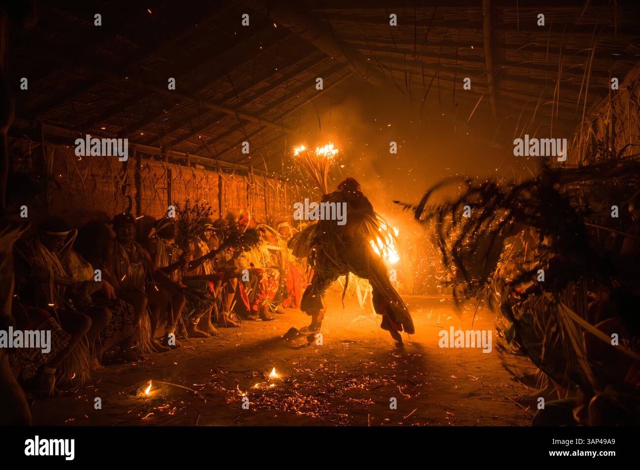 Les participants à une cérémonie des Bwiti, vêtus d'une tenue rituelle faite de feuilles de palmier séchées, dansent avec des torches allumées à l'intérieur d'un petit temple. Banque D'Images