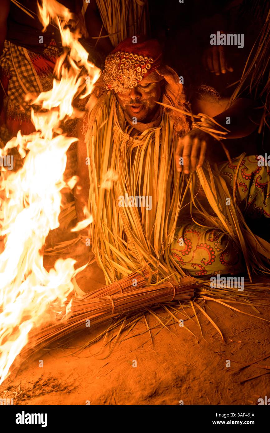 Participant à une cérémonie Bwiti, vêtu d'un costume rituel fait de feuilles de palmier séchées, préparant le feu pour commencer sa danse. Banque D'Images