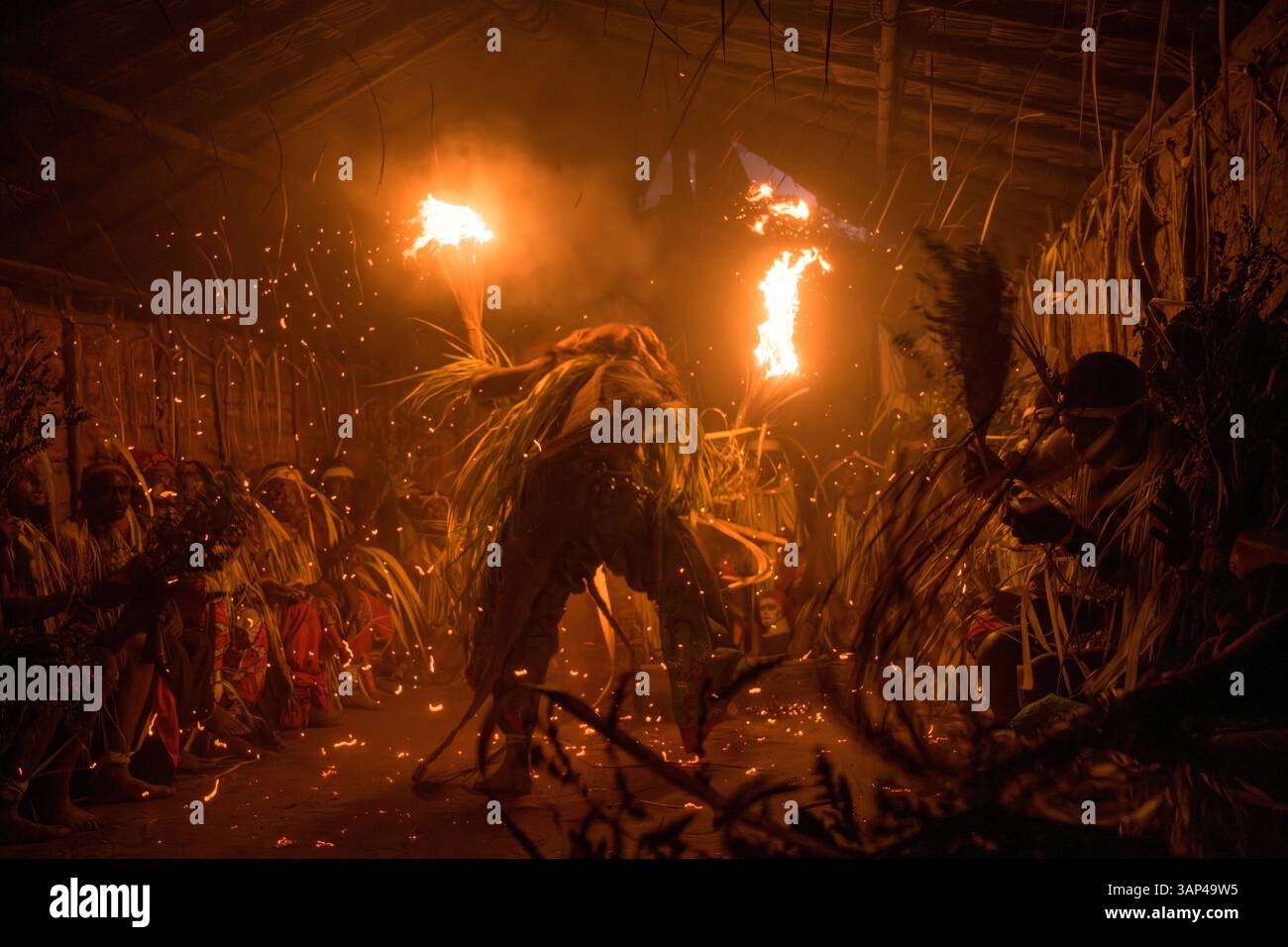 Les participants à une cérémonie des Bwiti, vêtus d'une tenue rituelle faite de feuilles de palmier séchées, dansent avec des torches allumées à l'intérieur d'un petit temple. Banque D'Images