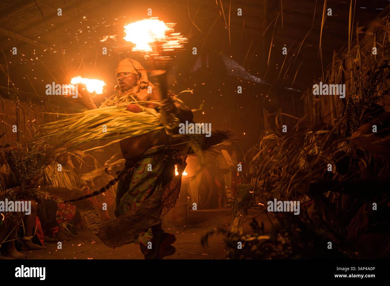 Les participants à une cérémonie des Bwiti, vêtus d'une tenue rituelle faite de feuilles de palmier séchées, dansent avec des torches allumées à l'intérieur d'un petit temple. Banque D'Images