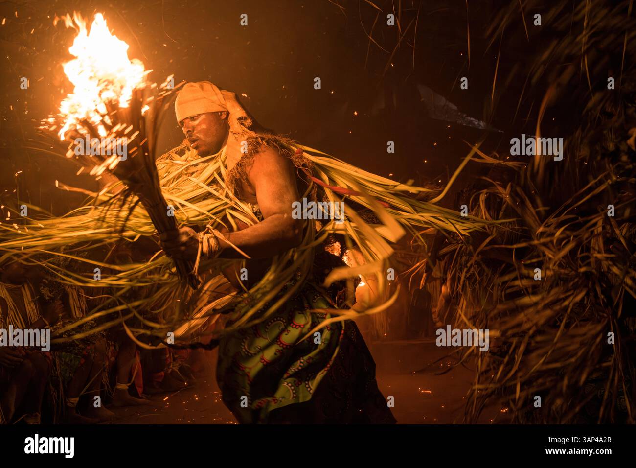 Les participants à une cérémonie des Bwiti, vêtus d'une tenue rituelle faite de feuilles de palmier séchées, dansent avec des torches allumées à l'intérieur d'un petit temple. Banque D'Images