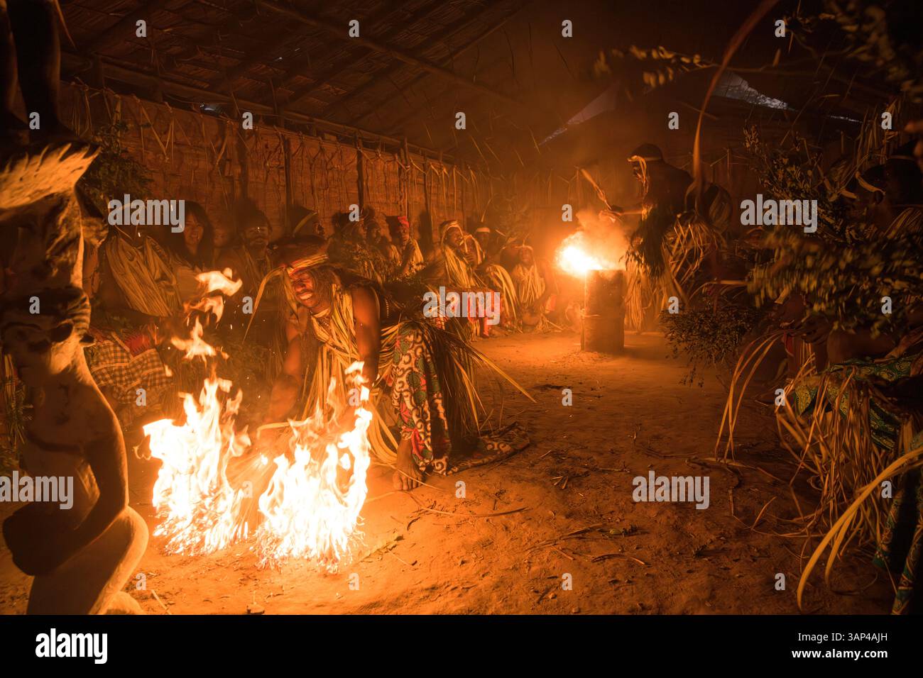 Les participants à une cérémonie des Bwiti, vêtus d'une tenue rituelle faite de feuilles de palmier séchées, dansent avec des torches allumées à l'intérieur d'un petit temple. Banque D'Images