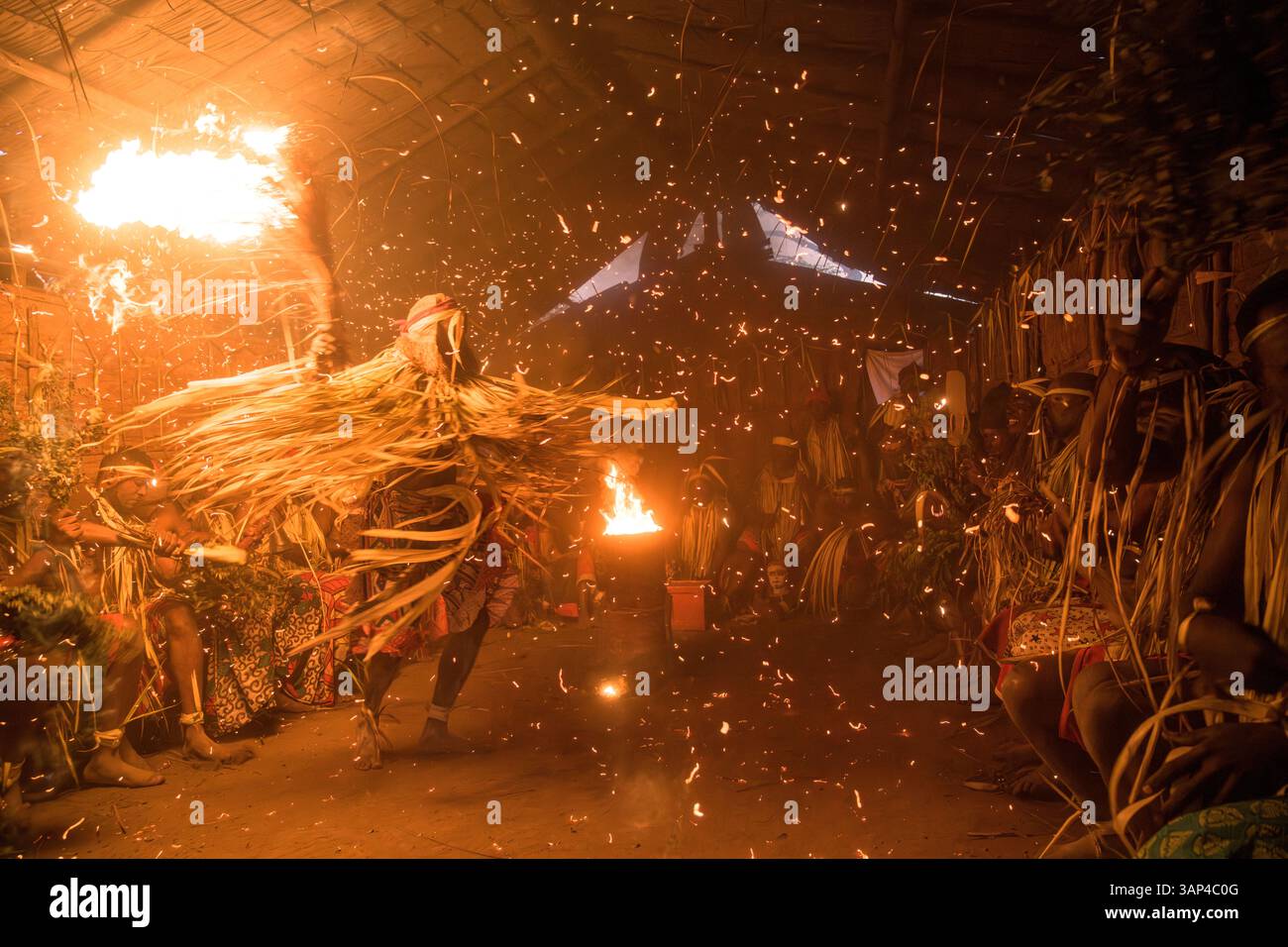 Les participants à une cérémonie des Bwiti, vêtus d'une tenue rituelle faite de feuilles de palmier séchées, dansent avec des torches allumées à l'intérieur d'un petit temple. Banque D'Images