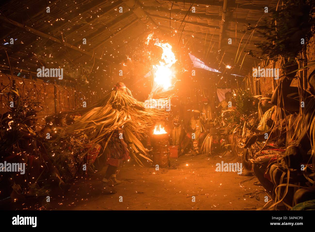 Les participants à une cérémonie des Bwiti, vêtus d'une tenue rituelle faite de feuilles de palmier séchées, dansent avec des torches allumées à l'intérieur d'un petit temple. Banque D'Images
