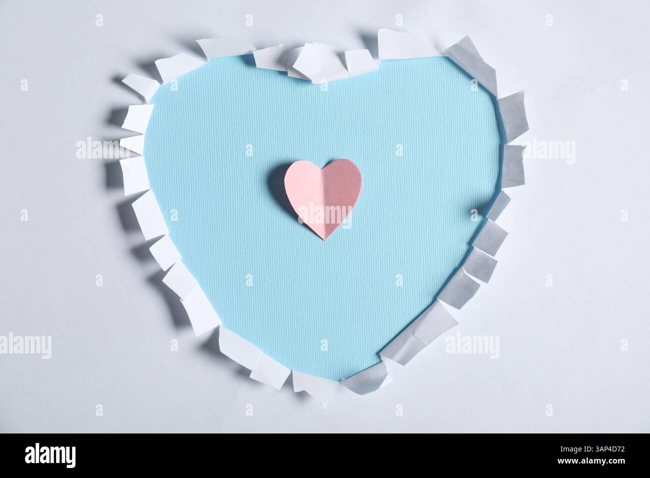 Papier blanc avec trou en forme de coeur et rose sur fond bleu clair, vue de dessus Banque D'Images