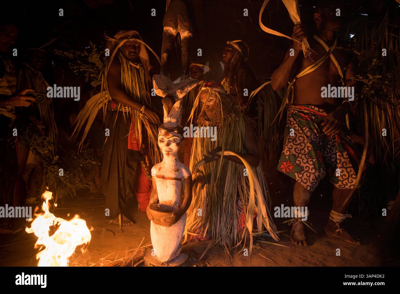 Les participants à une cérémonie des Bwiti, vêtus d'une tenue rituelle, dansent avec des torches allumées à l'intérieur d'un petit temple près du totem. Banque D'Images