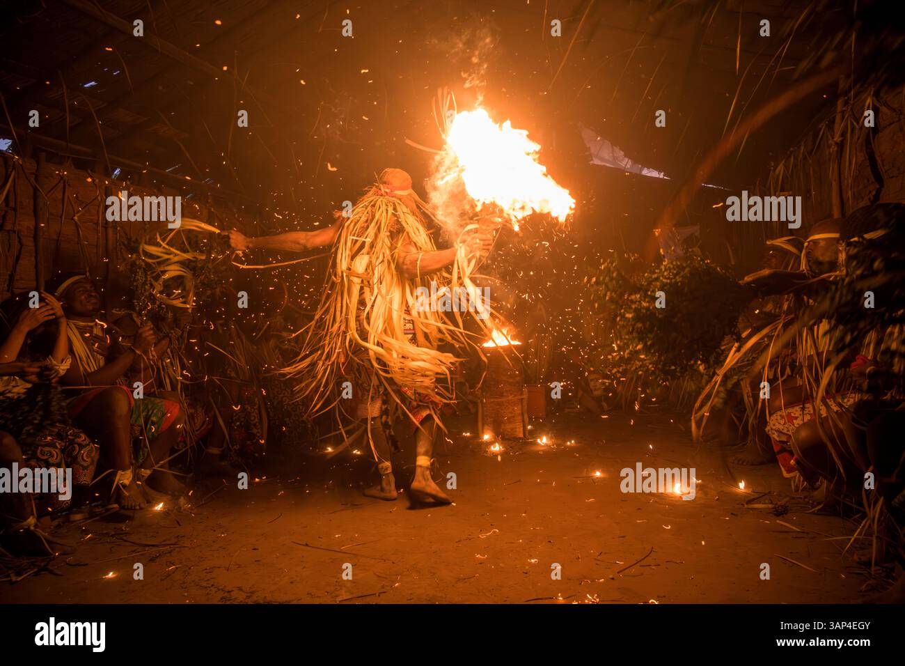 Les participants à une cérémonie des Bwiti, vêtus d'une tenue rituelle faite de feuilles de palmier séchées, dansent avec des torches allumées à l'intérieur d'un petit temple. Banque D'Images