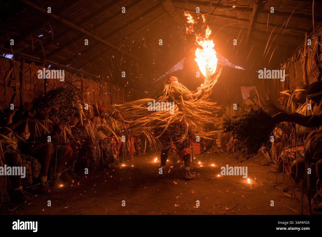 Les participants à une cérémonie des Bwiti, vêtus d'une tenue rituelle faite de feuilles de palmier séchées, dansent avec des torches allumées à l'intérieur d'un petit temple. Banque D'Images