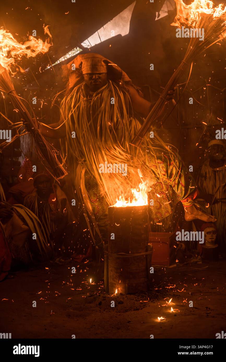 Les participants à une cérémonie des Bwiti, vêtus d'une tenue rituelle faite de feuilles de palmier séchées, dansent avec des torches allumées à l'intérieur d'un petit temple. Banque D'Images