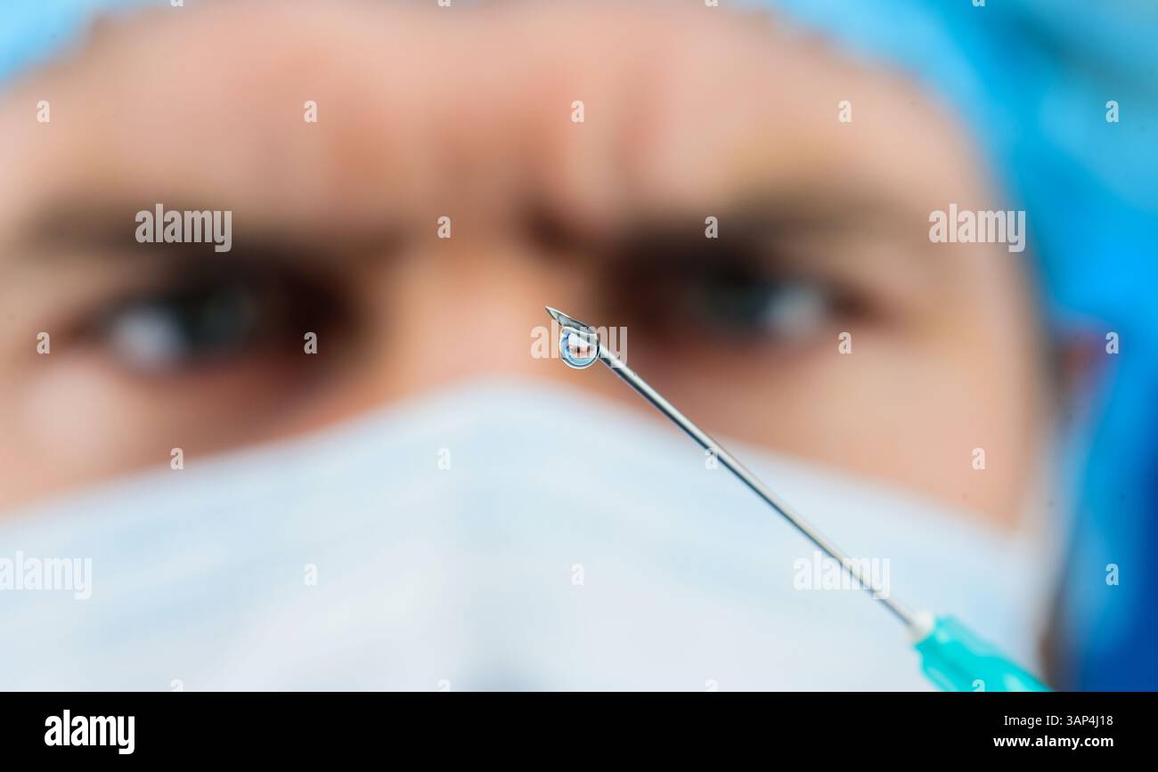 Vaccination. Médecin masculin professionnel dans le masque médical avec seringue se préparant à l'injection. Gros plan d'une goutte de médicament liquide ou de médicament sur la seringue Banque D'Images