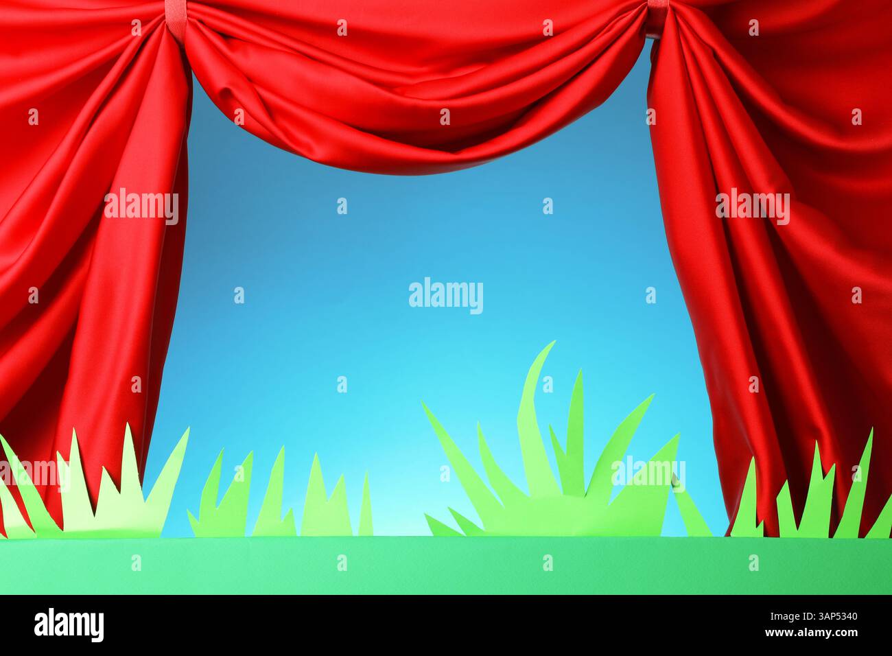 Spectacle de marionnettes. Scène verte vide avec des décorations et des rideaux rouges sur fond bleu clair Banque D'Images