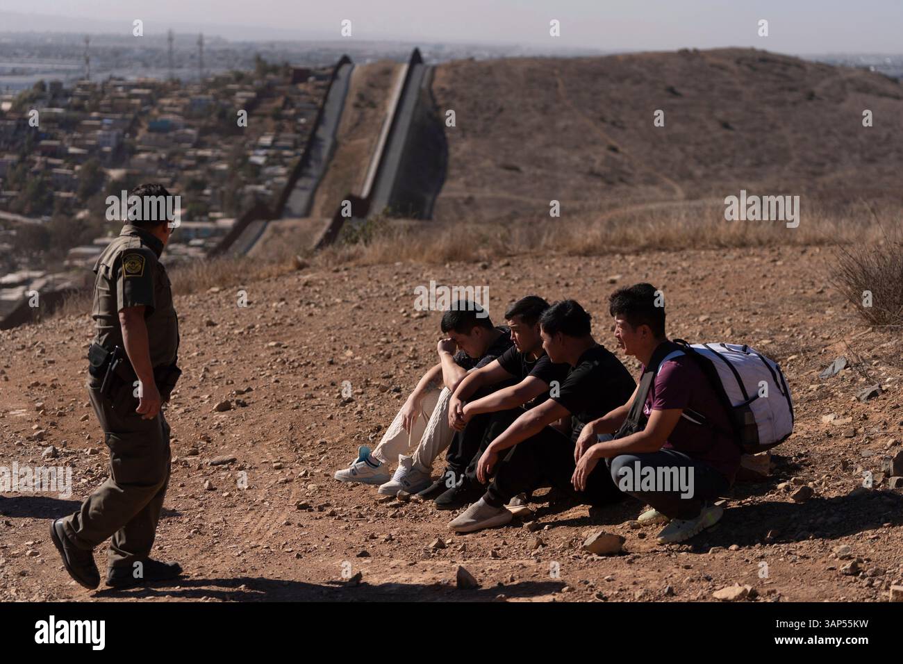 A Border Patrol agent walks past four men being detained after crossing the border illegally through a gap in the walls separating Mexico and the United States, Jan. 23, 2025, in San Diego. (AP Photo/Gregory Bull) Banque D'Images
