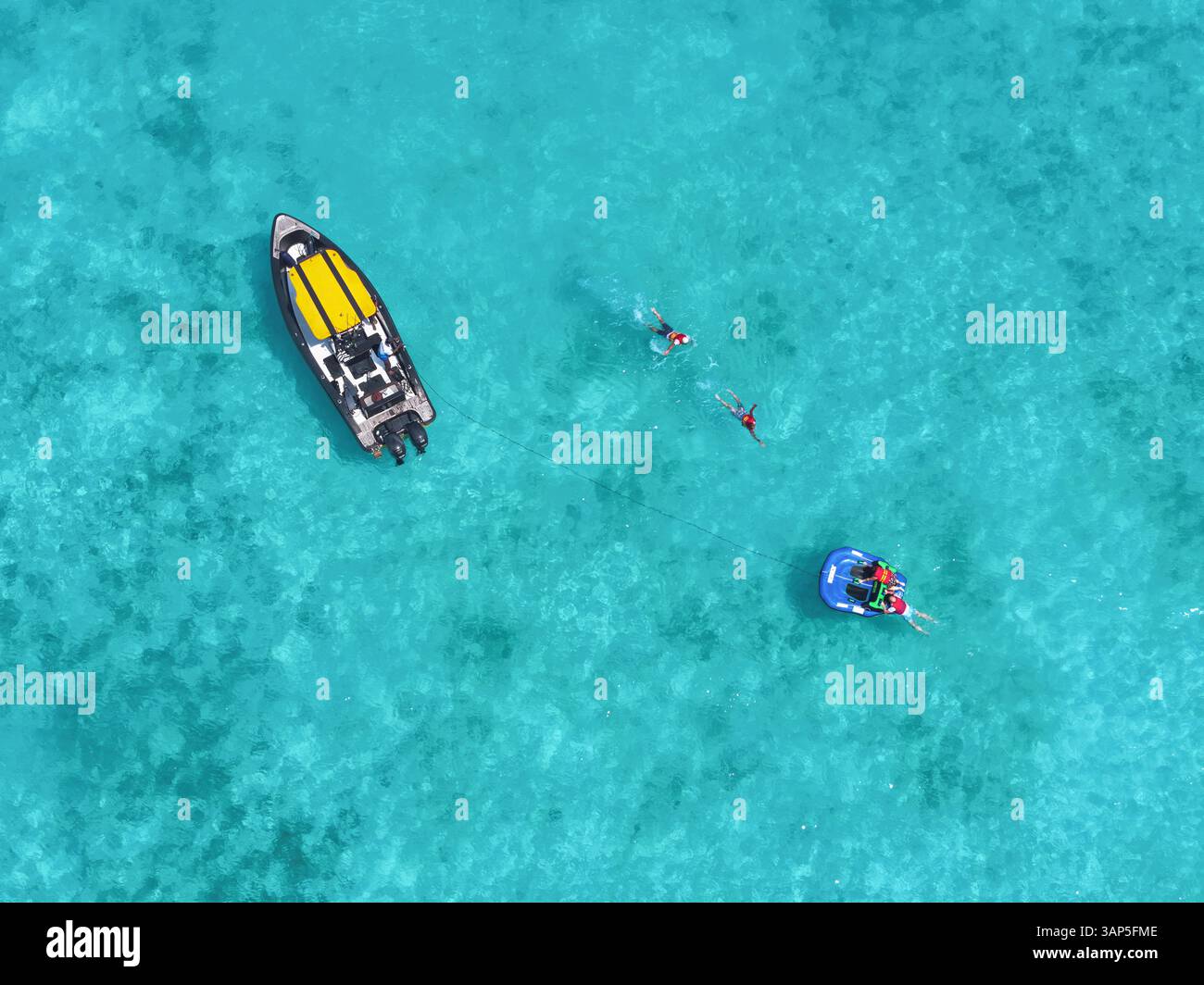 Vue aérienne de personnes pratiquant des sports nautiques sur un funtube derrière un bateau dans une eau turquoise claire avec de beaux coraux, Vashafaru, Haa Alif, Maldives. Banque D'Images