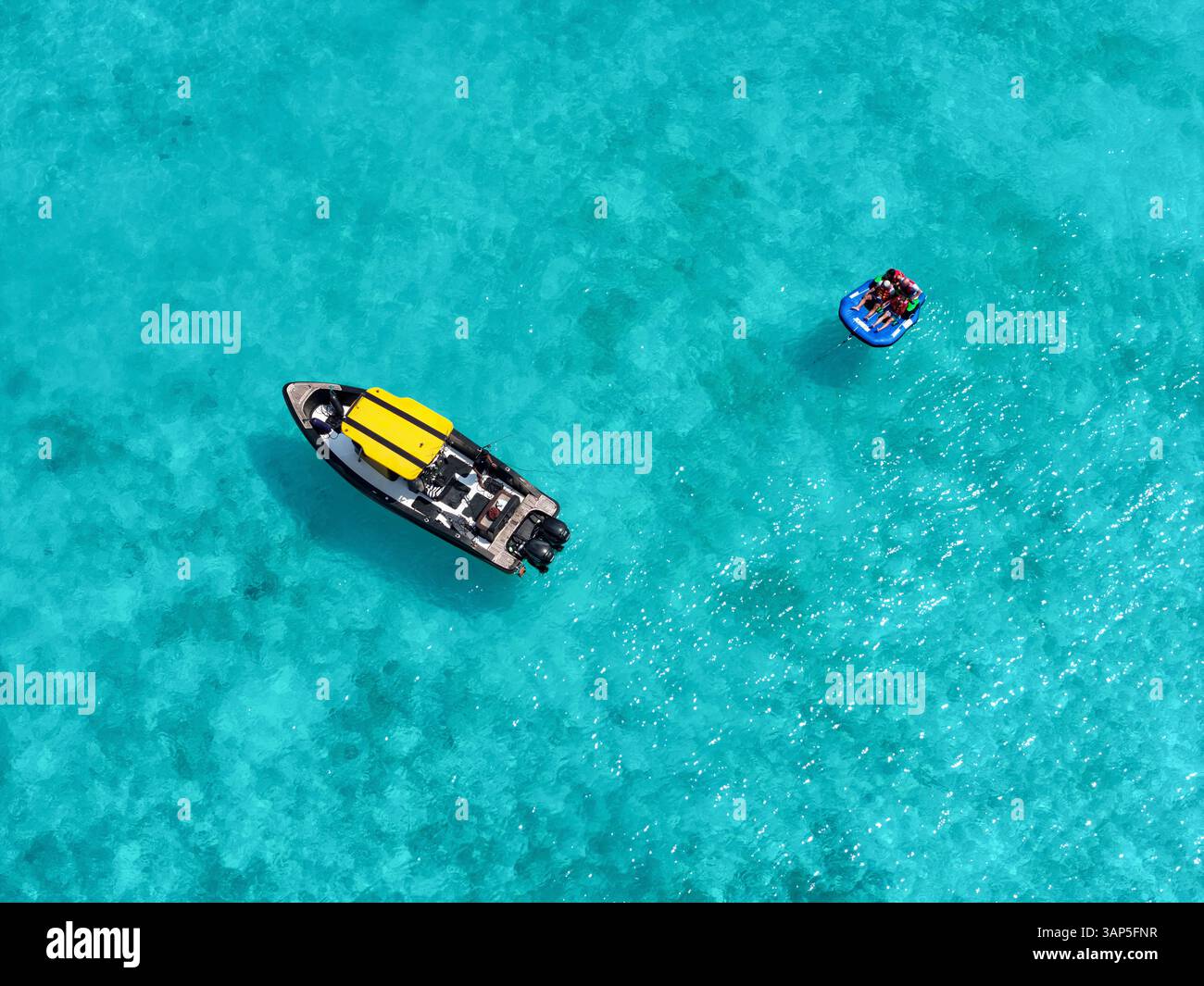 Vue aérienne des gens profitant d'un funtube derrière un bateau sur des eaux turquoises claires avec des coraux vibrants, Vashafaru, Haa Alif, Maldives. Banque D'Images