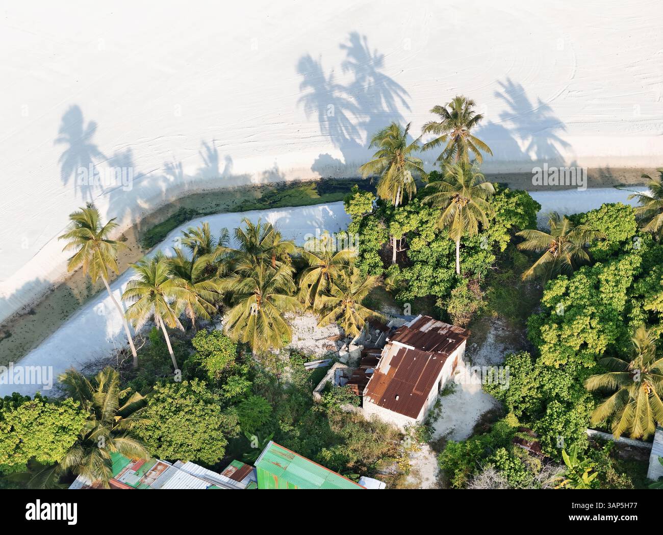 Vue aérienne de l'île tropicale avec des palmiers, du sable et des maisons sous un ciel ensoleillé, Maradhoo, Maldives. Banque D'Images