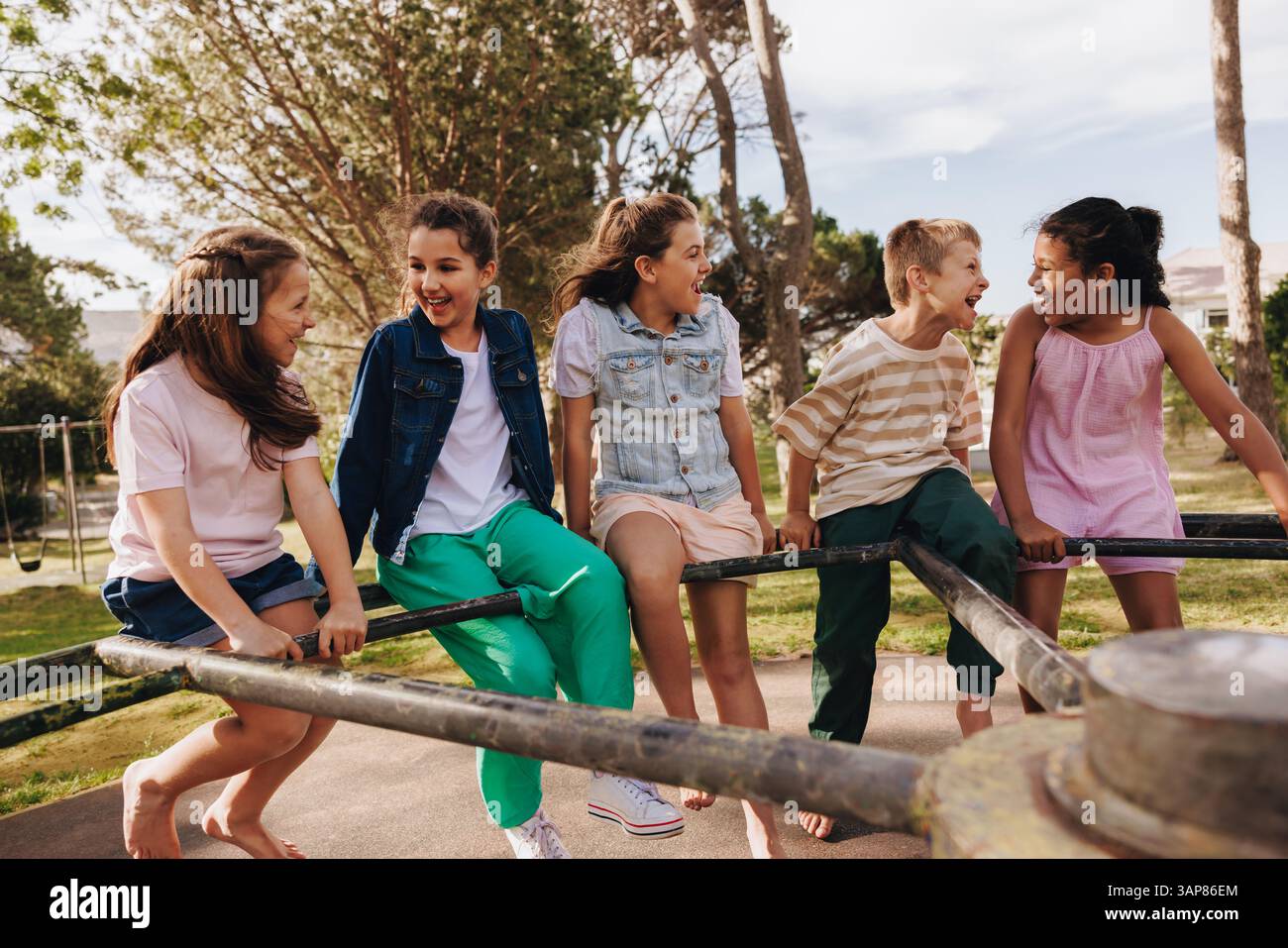 Un groupe joyeux d'enfants riant et jouant sur une aire de jeux dans un cadre de parc ensoleillé, appréciant l'amitié et l'activité de plein air, en se concentrant sur l'enfant Banque D'Images