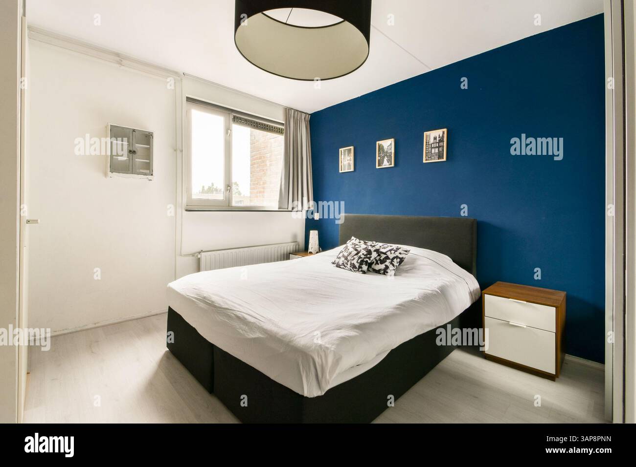 Une chambre simple mais élégante avec un lit confortable, un décor minimaliste et un mur d'accent bleu saisissant. Parfait pour les espaces de vie modernes. Banque D'Images