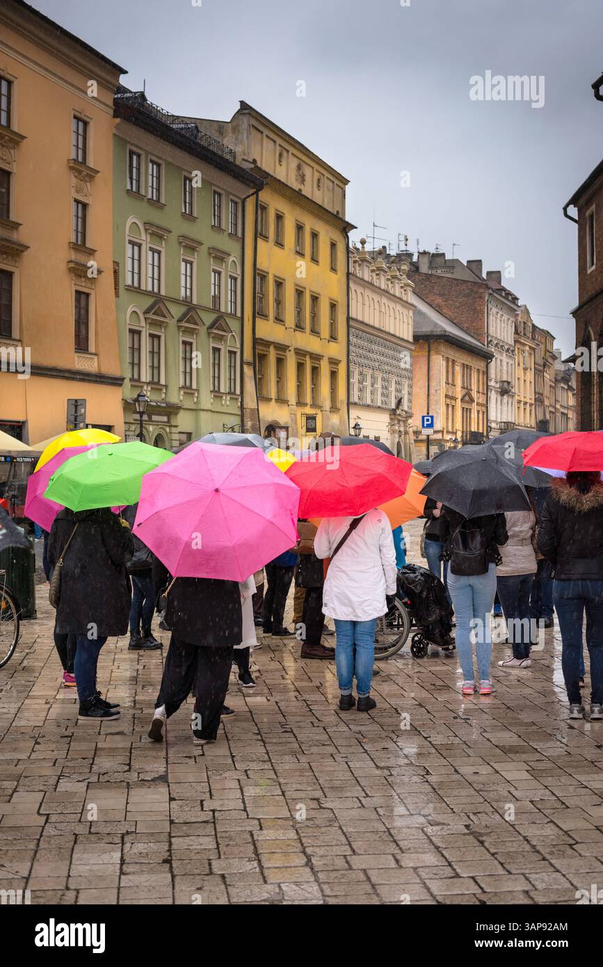 Touristes pluie parasols Europe, vue d'un groupe de touristes écoutant leur guide pendant le mauvais temps sur la place du Grand marché à Cracovie, en Pologne. Banque D'Images