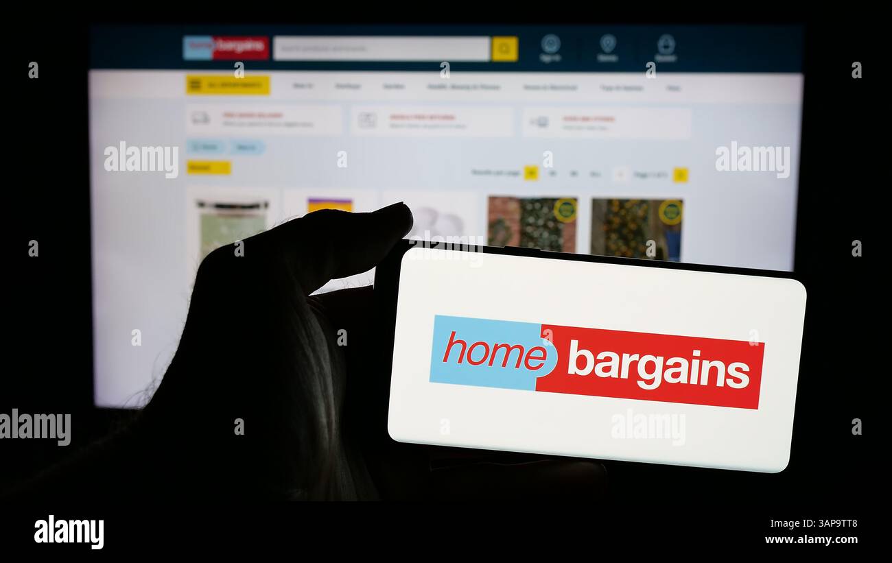 5 mars 2025, Allemagne : dans cette illustration photo, une personne tient un téléphone portable avec le logo de la société britannique T.J. Morris Limited (Home Bargains) sur l'écran devant la page Web de l'entreprise. (Crédit image : © timon Schneider/SOPA images via ZUMA Press Wire) USAGE ÉDITORIAL SEULEMENT ! Non destiné à UN USAGE commercial ! Banque D'Images