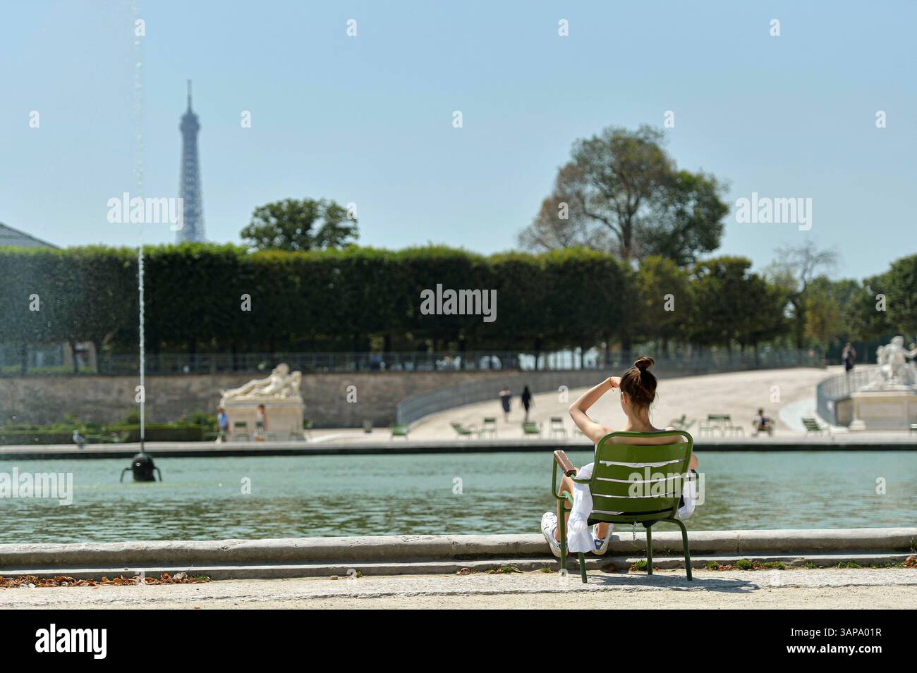 Paris (France) : femme vue de derrière, assise sur une chaise, dans le jardin botanique du jardin des Tuileries. Femme profitant du soleil devant un pon Banque D'Images