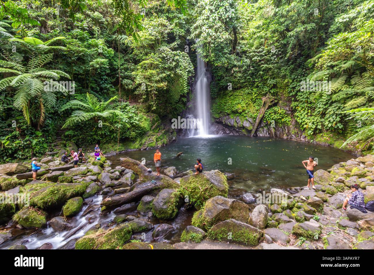 Les randonneurs se reposent sur les rochers avec Malabsay Falls en arrière-plan entouré par une végétation forestière luxuriante à Bicol, Philippines Banque D'Images