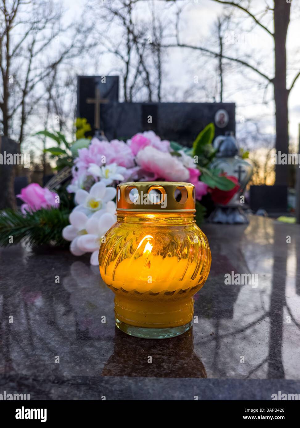 Bougie de deuil jaune éclatante assis sur une pierre tombale de granit sombre dans un cimetière. Banque D'Images