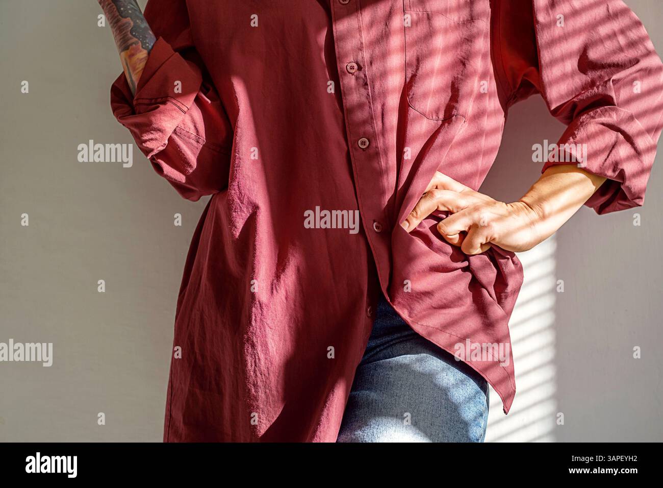 Femme recadrée dans la chemise Maroon pose avec la main sur la hanche, l'éclairage artistique accentue son style. Banque D'Images