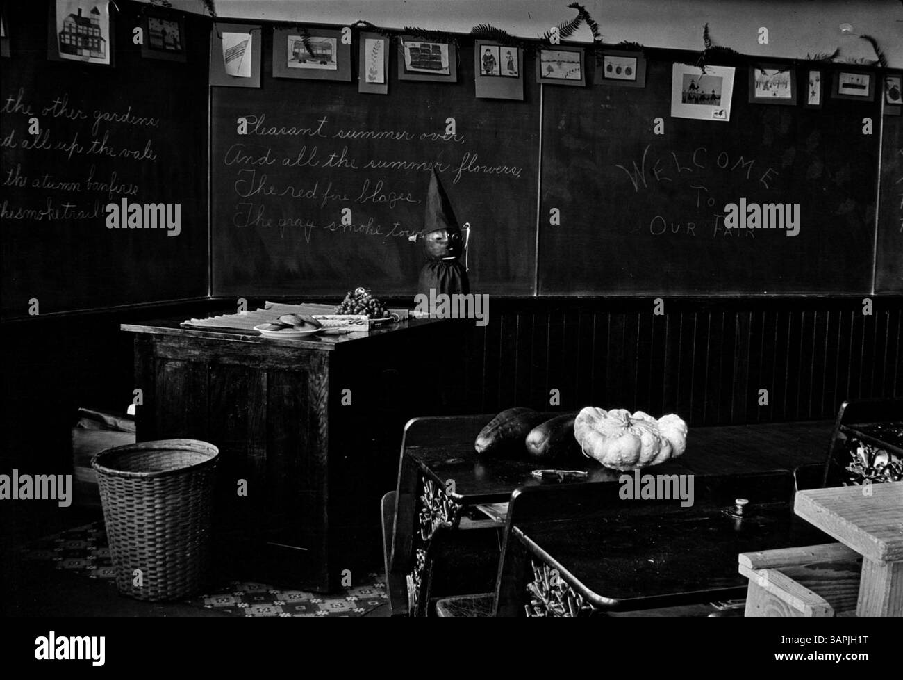 Photographie en noir et blanc par Roy C. Andrews d'une salle de classe décorée pour une foire à l'école Latham. Le tableau noir est orné de dessins et de fougères, et un bureau de professeur est visible avec des assiettes de nourriture et des œuvres d'art pour enfants. Banque D'Images