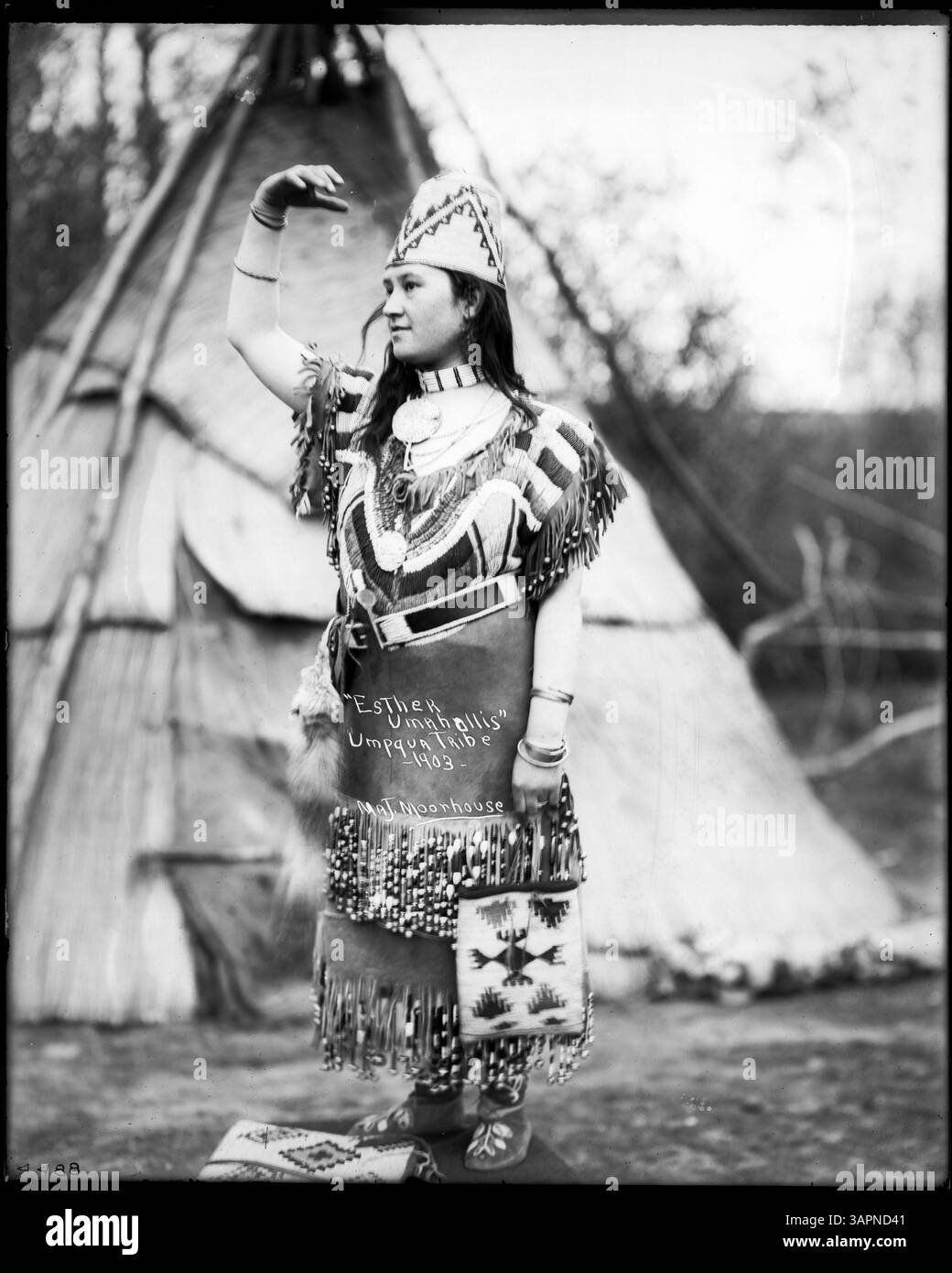 Photographie de Lee Moorhouse montrant Esther Umahollis, une femme tribale Umpqua, en regalia à côté d'un tipi, qui fait partie de la collection des bibliothèques de l'Université de l'Oregon. L'image reflète le patrimoine culturel indigène et les vêtements traditionnels. Banque D'Images