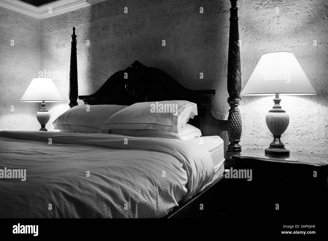 photographie en noir et blanc d'un lit double avec literie blanche de chaque côté du lit est une lampe de chevet allumée, le lit a un vintag en bois de style espagnol Banque D'Images