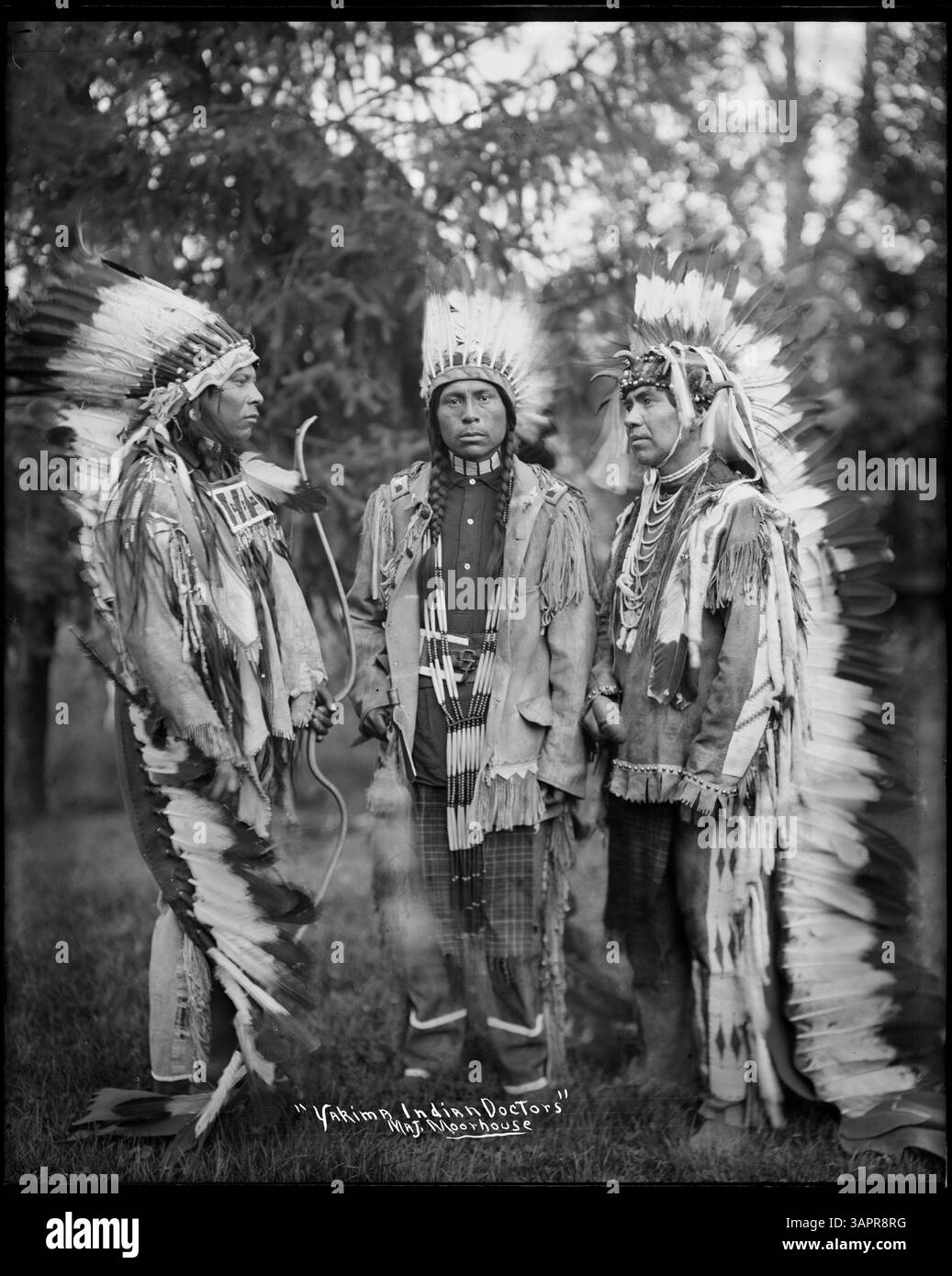 Cette photographie de Lee Moorhouse représente trois médecins indiens Yakima portant des bonnets de guerre, tenant des instruments médicaux. L'image capture l'importance culturelle de ces objets traditionnels et le rôle des hommes de médecine indigène. Banque D'Images