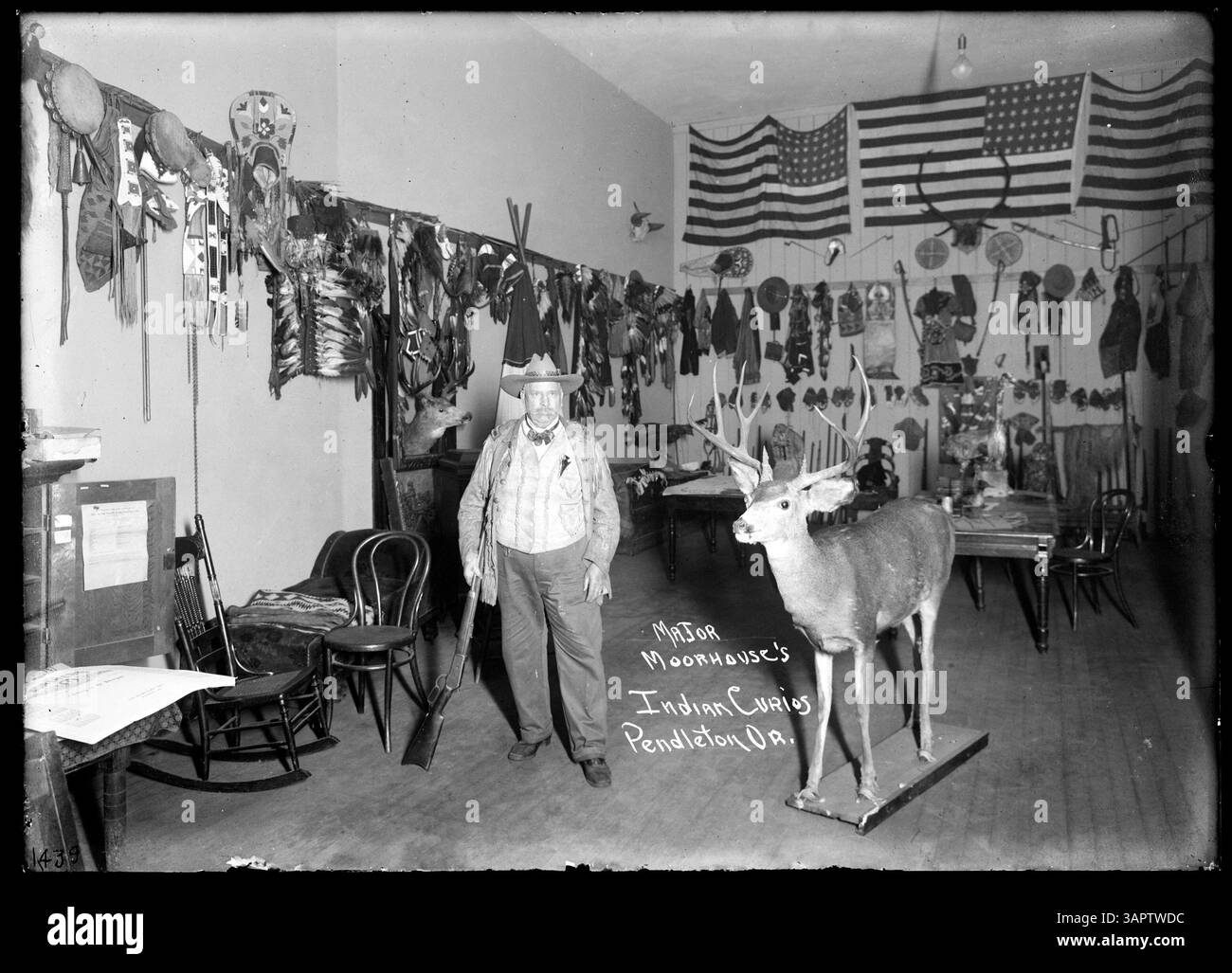 Cet autoportrait de Lee Moorhouse, pris vers 1915, le montre dans son bureau à Pendleton, Oregon. Entouré de ses « curiosités indiennes », Moorhouse pose avec un fusil à côté d'un buck en peluche, vêtu d'un gilet et en peau de sarrasin. Banque D'Images
