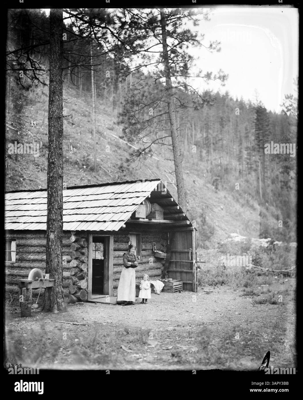 Photographie de Lee Moorhouse montrant une cabane de bûcheron, avec une femme et un enfant dans les environs à Huron, Oregon. Cette image fait partie de la collection PH036. Banque D'Images