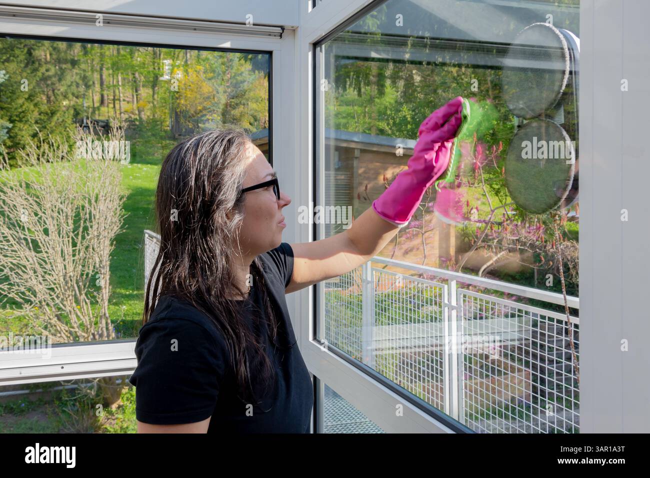 Une femme essuie manuellement une fenêtre tandis qu'un robot nettoyeur travaille à proximité Banque D'Images