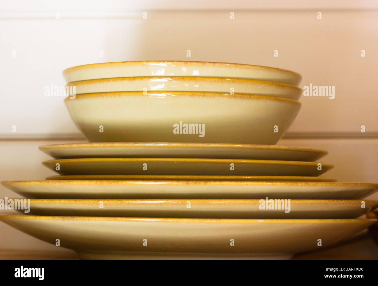 Une pile d'assiettes et de bols avec un ton rustique et chaleureux sont disposés, prêts pour une décoration à manger ou à la maison. Une pile de vaisselle de couleur crème sur une étagère. Banque D'Images
