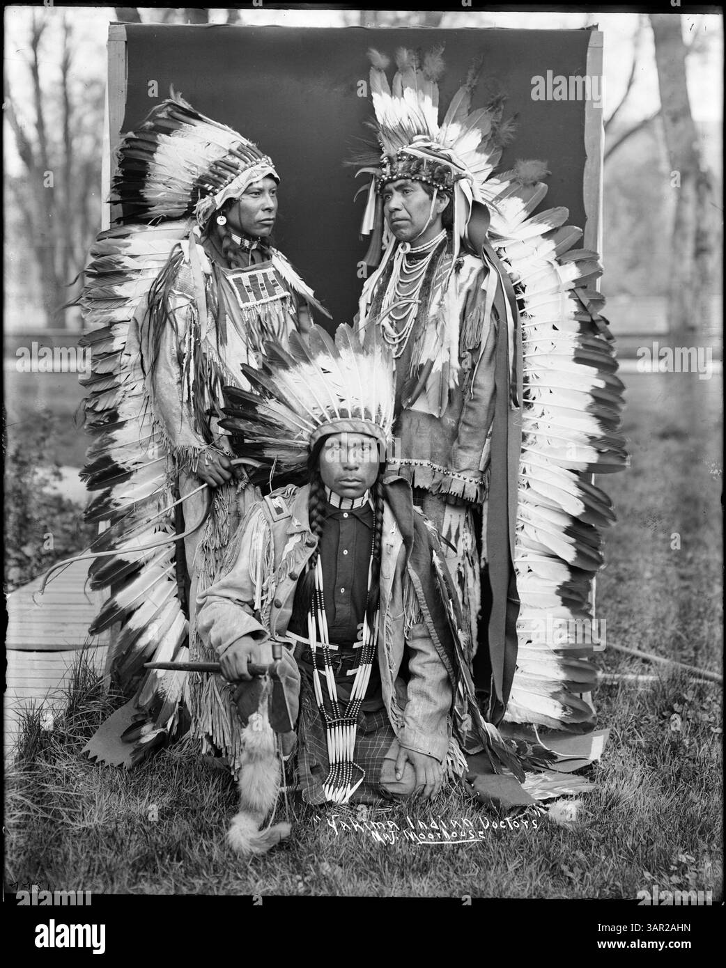 Cette photographie de Lee Moorhouse montre trois médecins indiens Yakima portant des bonnets de guerre, chacun portant des instruments médicaux, mettant en valeur des vêtements indigènes et des pratiques de guérison traditionnelles. Banque D'Images