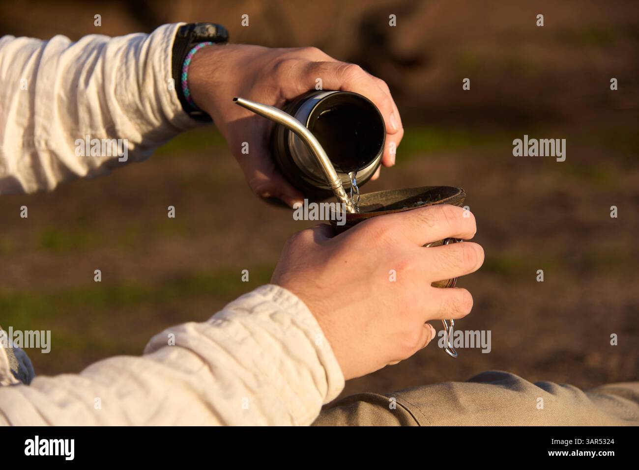 Une personne méconnaissable verse l'eau d'un thermos dans un compagnon, pour boire cette boisson traditionnelle Argentine. Banque D'Images