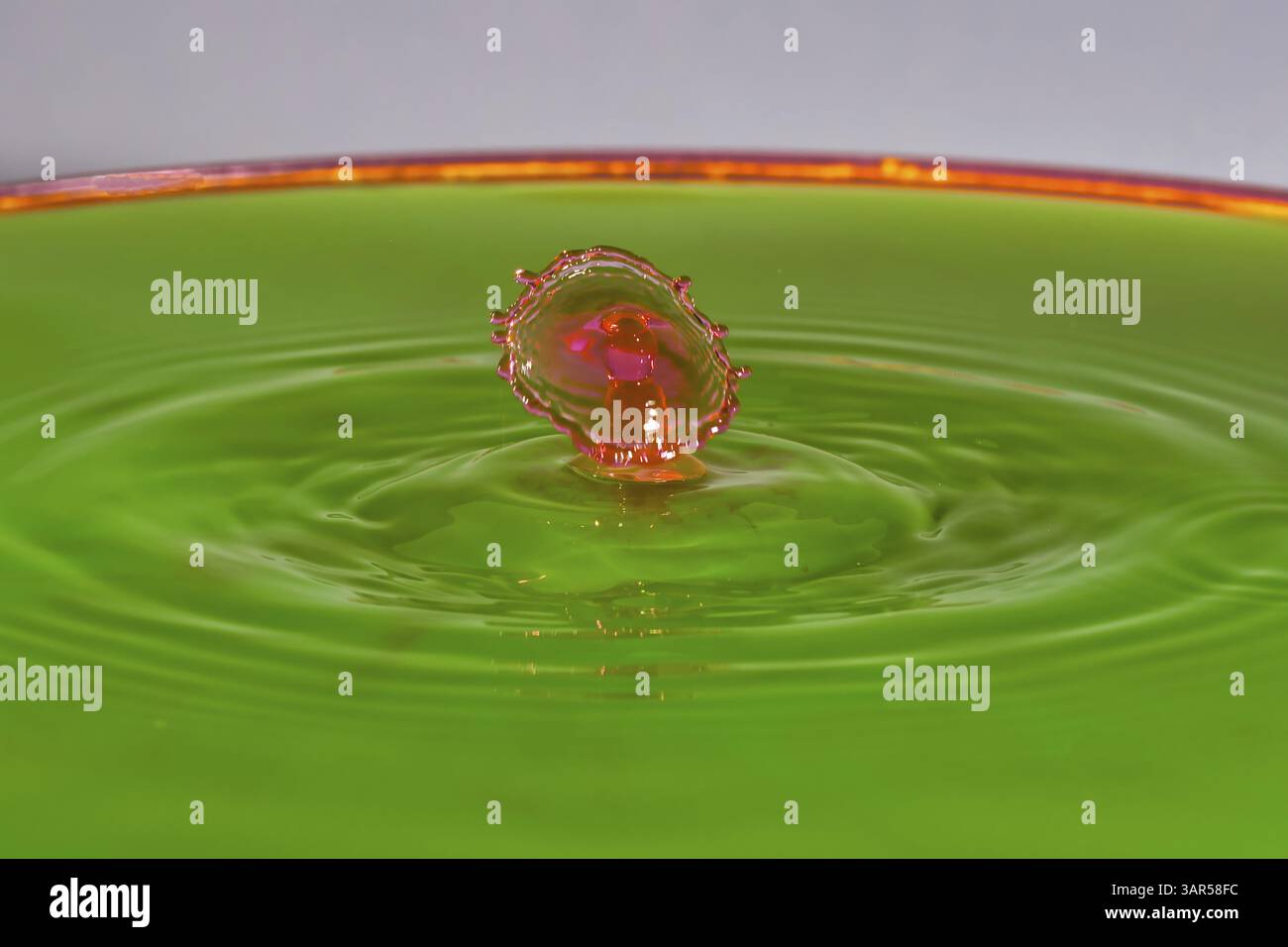 Une goutte rouge rencontre l'eau verte et crée des formes vives et des reflets, des gouttelettes d'eau, collision, photographie à grande vitesse, concept, chiffres de l'eau Banque D'Images